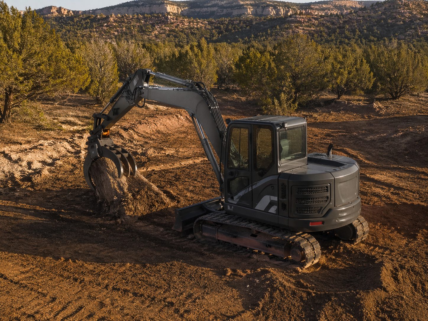 Compact tracked excavator with grapple attachment clearing stump on New Mexico mesa, Iron Attachments